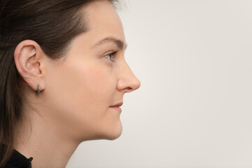 A woman with long brown hair poses gracefully in profile, revealing her facial features. The neutral background emphasizes her serene expression and elegance during the moment