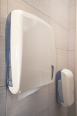 White dispenser for hand towels.In the background a dispenser for toilet paper.