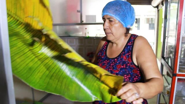 A latina woman cutting a plantain leaf to prepare Quesillo inside a kitchen in Yaguara, Huila, Colombia. Colombian food concept