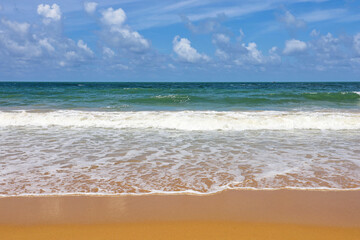 Empty sea beach with yellow sand, view to emerald green waves and blue sky with clouds