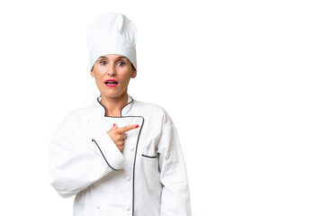 Middle-aged chef woman over isolated background surprised and pointing side