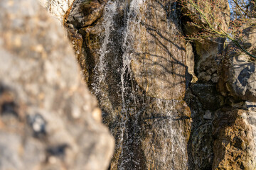 A waterfall is flowing down a rock. The water is spraying out of the rock. The water is white and clear