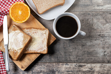 Sliced fresh bread with butter and coffee for breakfast on wooden table. Top view. Copy space
