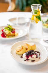 A plate features fluffy pancakes topped with berry compote and cream, presented elegantly. In the background, a refreshing water bottle with lemon and mint complements the meal.