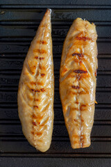 Smoked mackerel fillets cooking on a cast iron skillet griddle background backdrop.