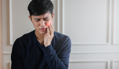 close up young asian man frown and use hand to massage on cheek after feeling pain or hurt from tmj...
