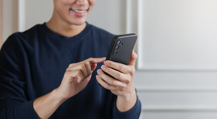 close up young asian man hand hold mobile cell phone device to play social media or read news...
