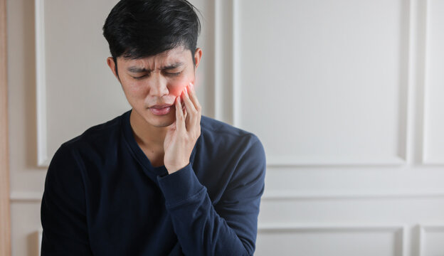 close up young asian man frown and use hand to massage on cheek after feeling pain or hurt from tmj muscle symptom at home for un healthy lifestyle and treatment concept