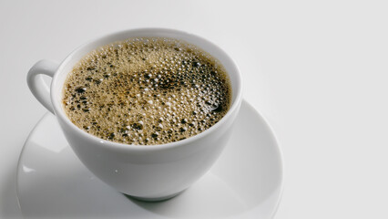 full single white coffee cup full with black coffee bubbles on surface isolated on white background, closeup and high angle view