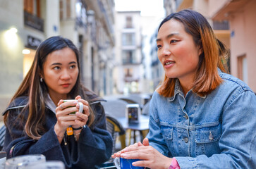 Two young women talking and drinking coffee at outdoor cafe