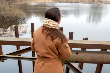 A young woman in brown coat standing on river shore