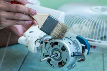 A man is cleaning a fan, including cleaning the propeller, the engine (and providing lubricants), and cleaning the fan guard grill