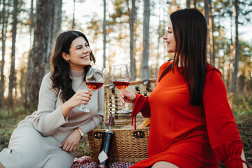 Two young caucasian woman have picnic drink wine in the forest	
