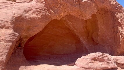 Natural red sandstone cave with textured walls under desert sun. Ancient rock formation creates dramatic shadowed space, desert cave mystery, desert cave texture, desert cave beauty.