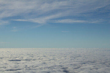 Aerial view above thick clouds, blue sky overhead.