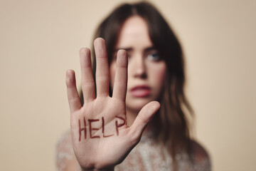 A woman speaks out against domestic violence by showing her hand with the word HELP written on it, symbolizing the need for support and awareness