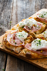 Pinsa Romana with mortadella, burrata cheese and pistachio on wooden table	