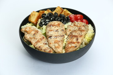 Loaded Caesar salad in black bowl: crispy protein, romaine, croutons, olives, tomatoes, creamy dressing on white