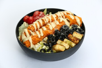 Loaded Caesar salad in black bowl: crispy protein, romaine, croutons, olives, tomatoes, creamy dressing on white