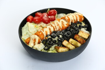 Loaded Caesar salad in black bowl: crispy protein, romaine, croutons, olives, tomatoes, creamy dressing on white