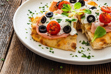 Pinsa Romana with mortadella, burrata cheese, black olives and cherry tomatoes on wooden table	
