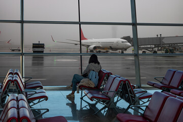 Obraz premium Silhouette of woman waiting for flight in the Airport-Busy airport airfield runway with group of airplanes queueing to departure heavy and fogy air traffic - istanbul airport, istanbul