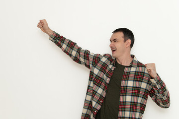 A man expresses joy and triumph with a raised fist. He is wearing a plaid shirt and a T-shirt...