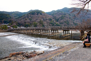 Picturesque scene with a japanese woman holding an umbrella and wearing a traditional japanese kimono - Togetsukyo Bridge in Arashiyama, Kyoto.