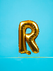 Close up of golden inflated balloon in the shape of letter R for entertainment and parties on blue...