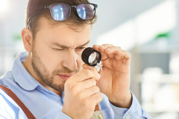 Close up of focused man closely examining diamond ring through magnifying loupe in studio....