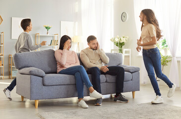 Mother and father sitting on sofa and being tired of their naughty children who are running around...