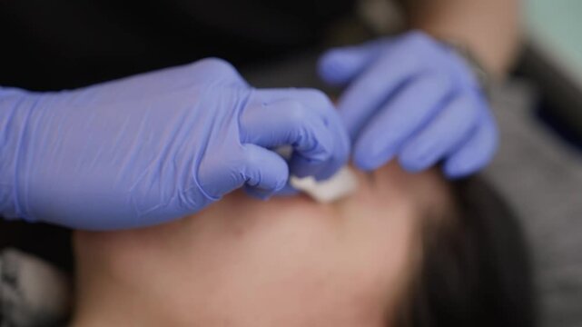 Beautician wearing blue gloves applying chemical peel to a woman's face, a cosmetic procedure for skin rejuvenation