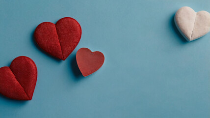Obraz premium Four fabric hearts in shades of red and white are arranged on a light blue background, with varying sizes and stitching details.