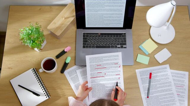 Top view of woman working on text for translation. Editor marks words in script on paper and laptop.