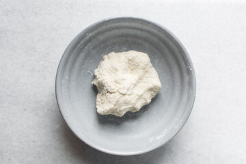 Overhead view of noodle dough being being mixed in a grey bowl, process of making hand pulled noodles