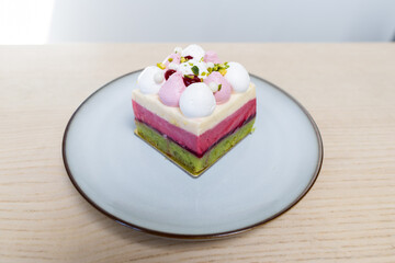 A plate of colorful three layers cake with creams on top.