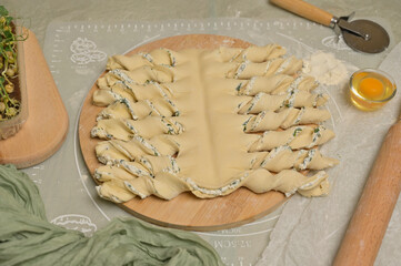 Twisted dough strips on wooden board. Cutter, egg, rolling pin, green towel, microgreens sprouts on kitchen table. Home cooking baking puffs
