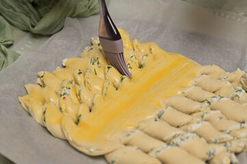 Close up smears yolk on the twisted dough strips with a brush. Parchment on kitchen table. Home cooking baking puffs