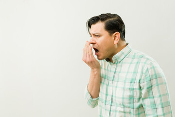 Latin male checking breath, hand covering mouth, expressing personal hygiene awareness and...