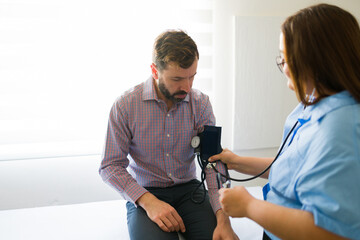 Nurse taking blood pressure of a male patient during medical consultation in a modern doctor's...