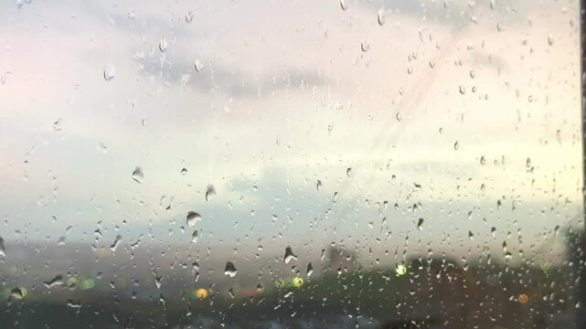 Slowly flowing raindrops on a window with a view of the evening city at sunset in high quality without camera movement