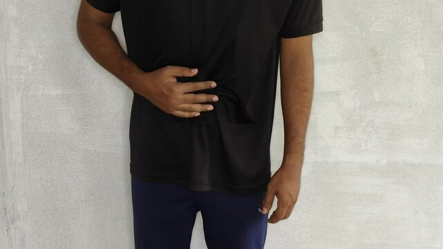 Young adult asian man with hand on stomach isolated on white background. Closeup view. Stomach ache, abdominal pain, diarrhea, food poisoning, upset belly, gas, cramp and appendicitis concept.