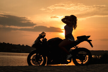 Fototapeta premium Woman biker at sunset, woman riding motorcycle, motorcycle driver travel, girl racing on beach road, freedom life