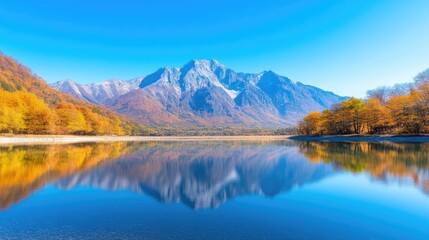 Obraz premium A serene lake reflects a snow-capped mountain range and autumnal trees. The composition is balanced, showcasing the mirrored image. High resolution and bright lighting enhance the scenes clarity. Th