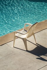 Fototapeta premium Empty white plastic chair by poolside on sunny day