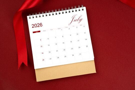 July 2026 desk calendar and red ribbon on red background.