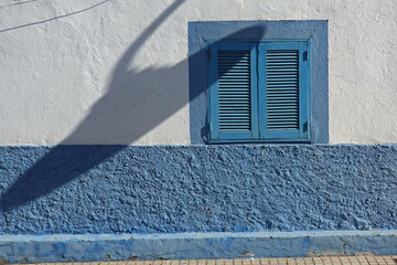 Window with shutters closed on white and blue wall.