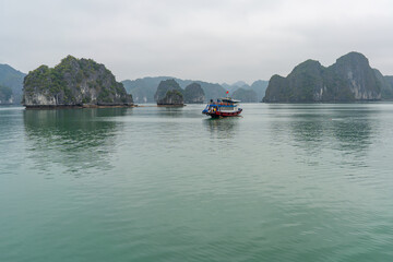 Fototapeta premium A boat cruises through the stunning seascape of Halong Bay, surrounded by natural wonders.