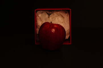 Red apples and red boxes on a black background, with dim lighting to simulate a chiaroscuro effect