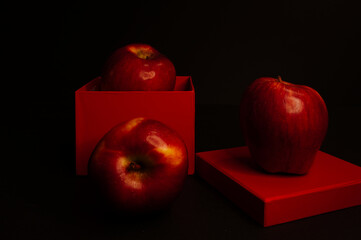 Red apples and red boxes on a black background, with dim lighting to simulate a chiaroscuro effect